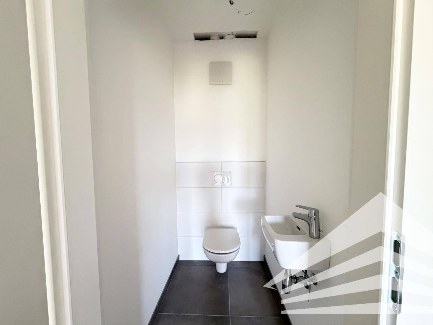 Kleines Gäste-WC mit wandhängender Toilette und Handwaschbecken, modern gefliest.