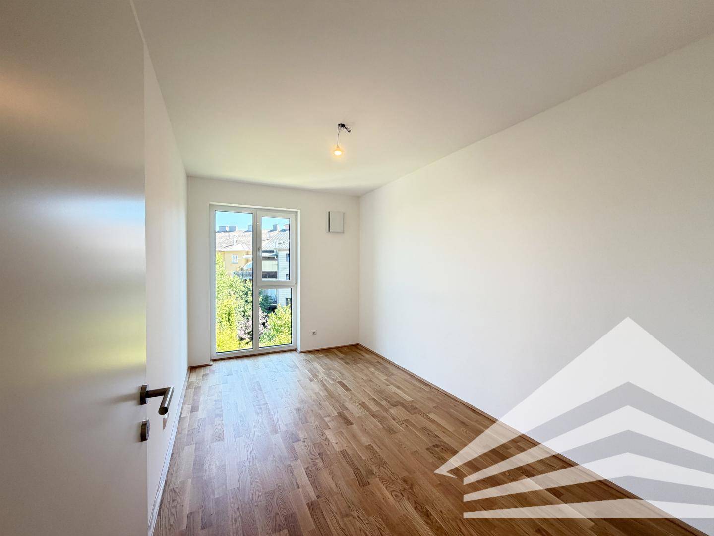 Helles Schlafzimmer mit Holzboden und großem Fenster, das viel Tageslicht hereinlässt.