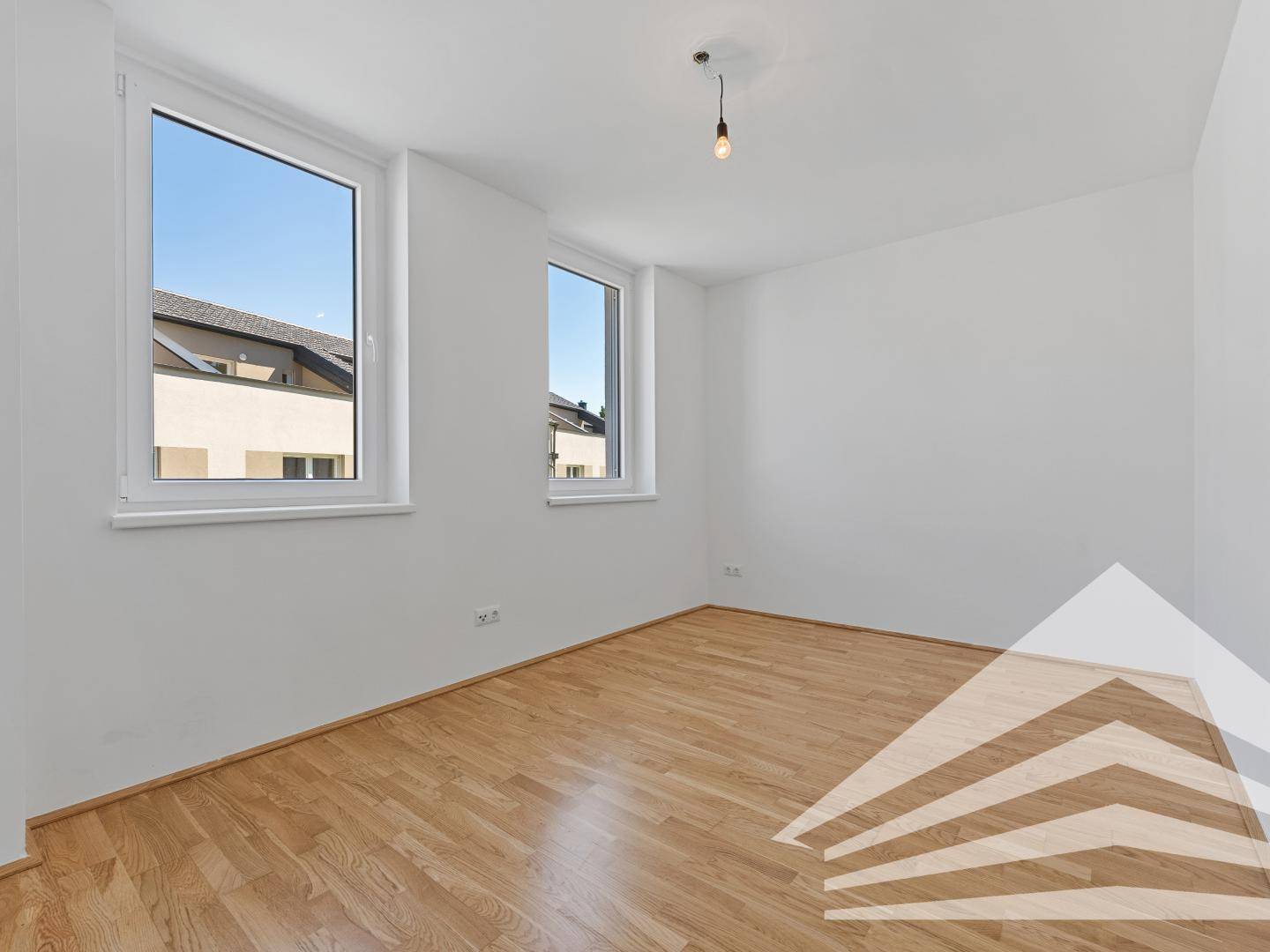 Helles Schlafzimmer mit Parkettboden und zwei Fenstern mit Blick nach draußen.