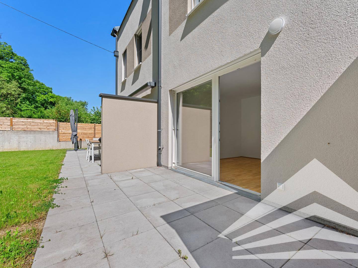 Sonniger Terrassenbereich mit Fliesenboden, Rasenfläche und direktem Zugang zum Haus.