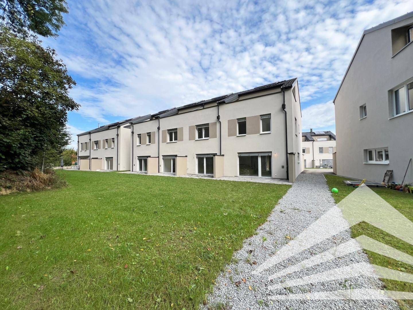 Reihenhäuser mit moderner Architektur, umgeben von Rasenflächen und einem Kiesweg.