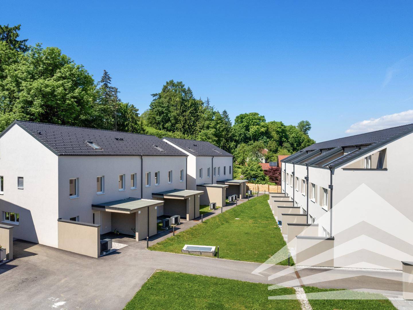 Moderne Reihenhäuser mit gepflegten Grünflächen unter blauem Himmel, umgeben von Bäumen.