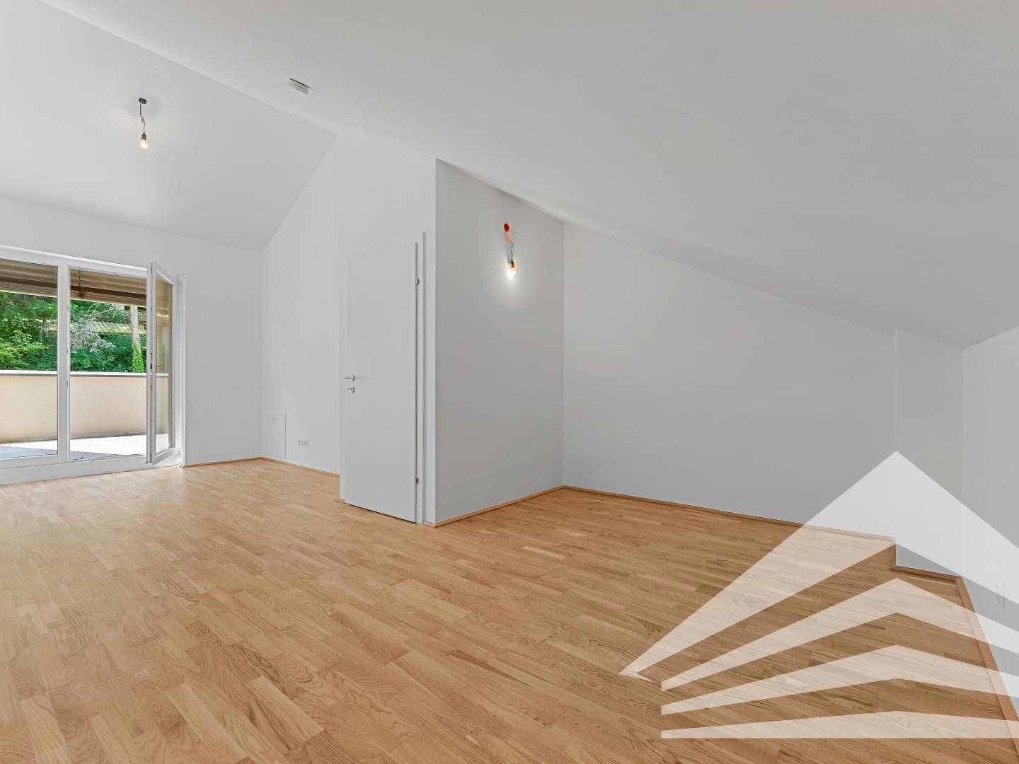 Helles Zimmer im Dachgeschoss mit schräger Decke, Parkettboden und Zugang zu einem Balkon.