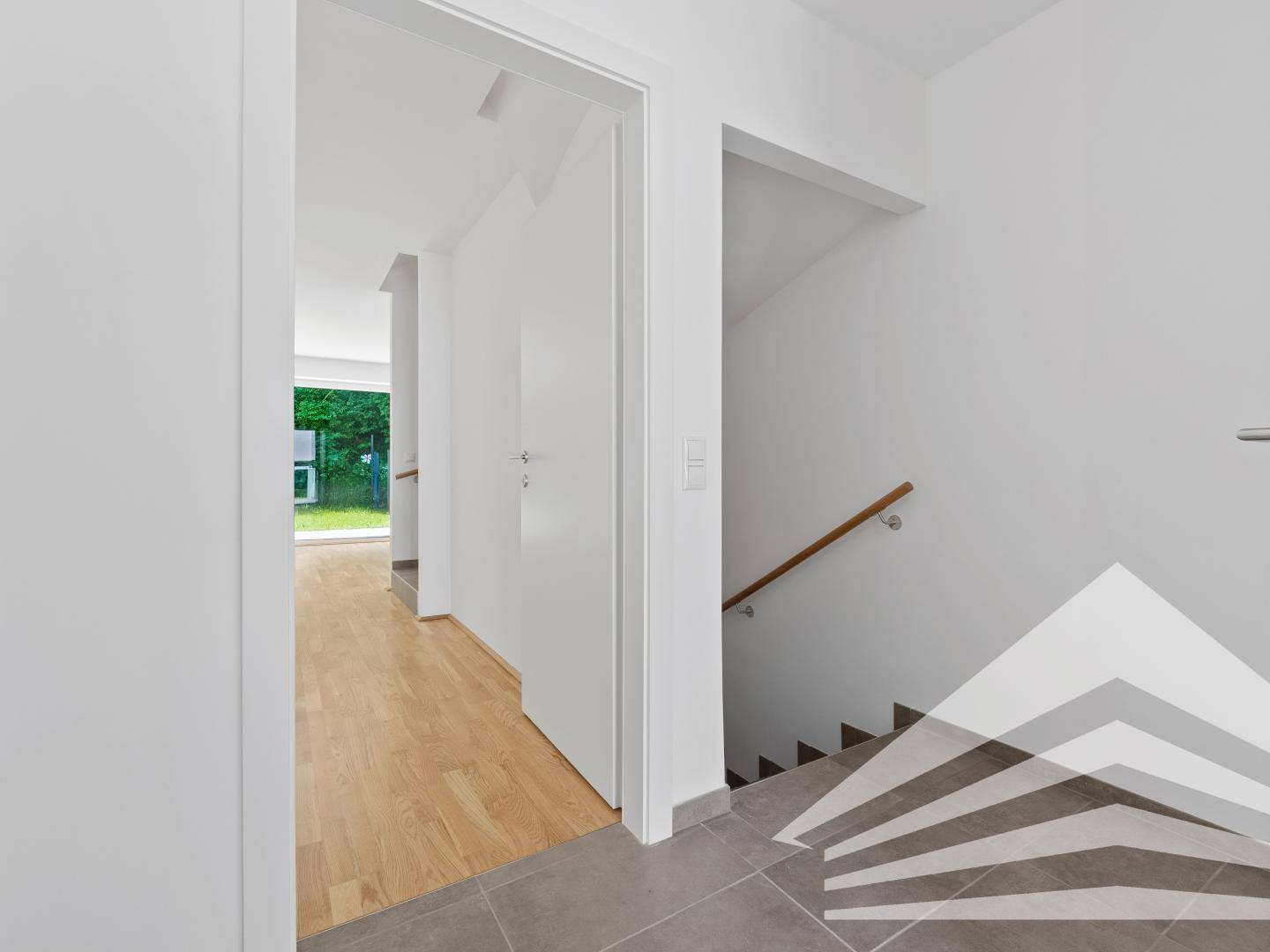 Heller Eingangsbereich mit Fliesenboden, Holztreppe und Zugang zu weiteren Räumen.