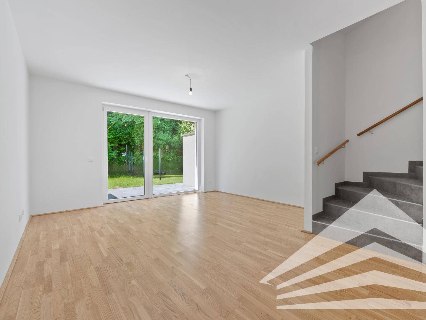 Helles Wohnzimmer mit Parkettboden, Zugang zur Terrasse und offener Treppe.