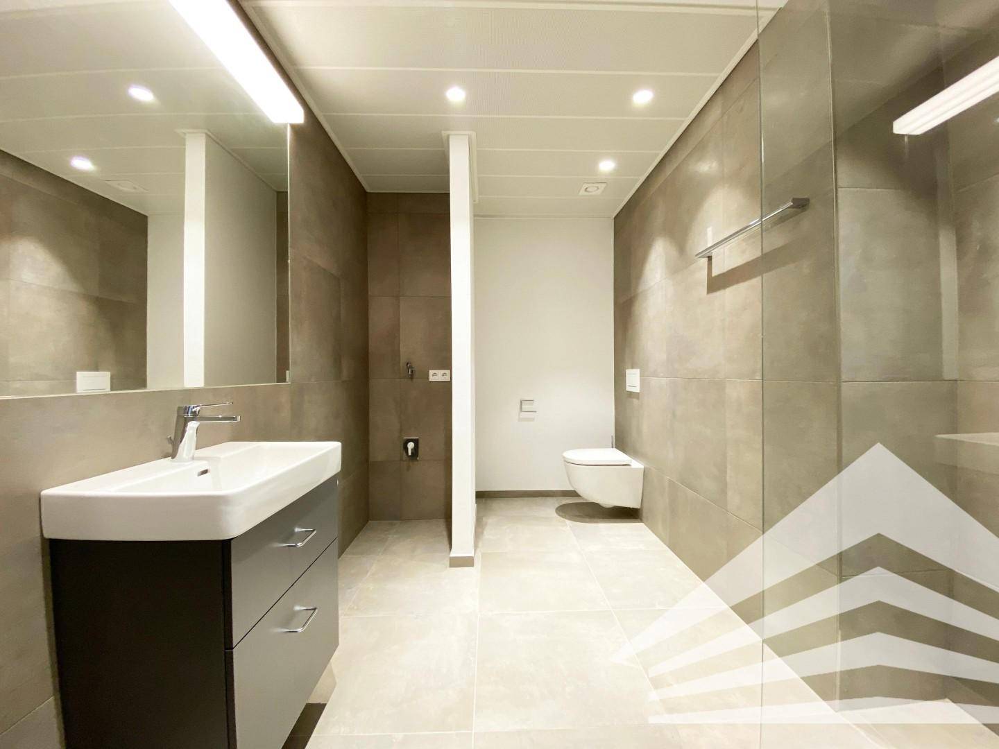 Modernes Badezimmer mit großen Fliesen, Waschtisch und wandhängendem WC.