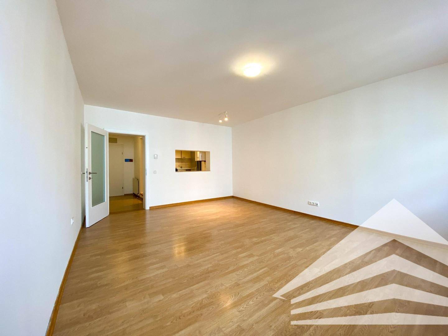 Geräumiges, leeres Wohnzimmer mit Holzboden und Durchreiche zur Küche, bereit zur individuellen Gestaltung.