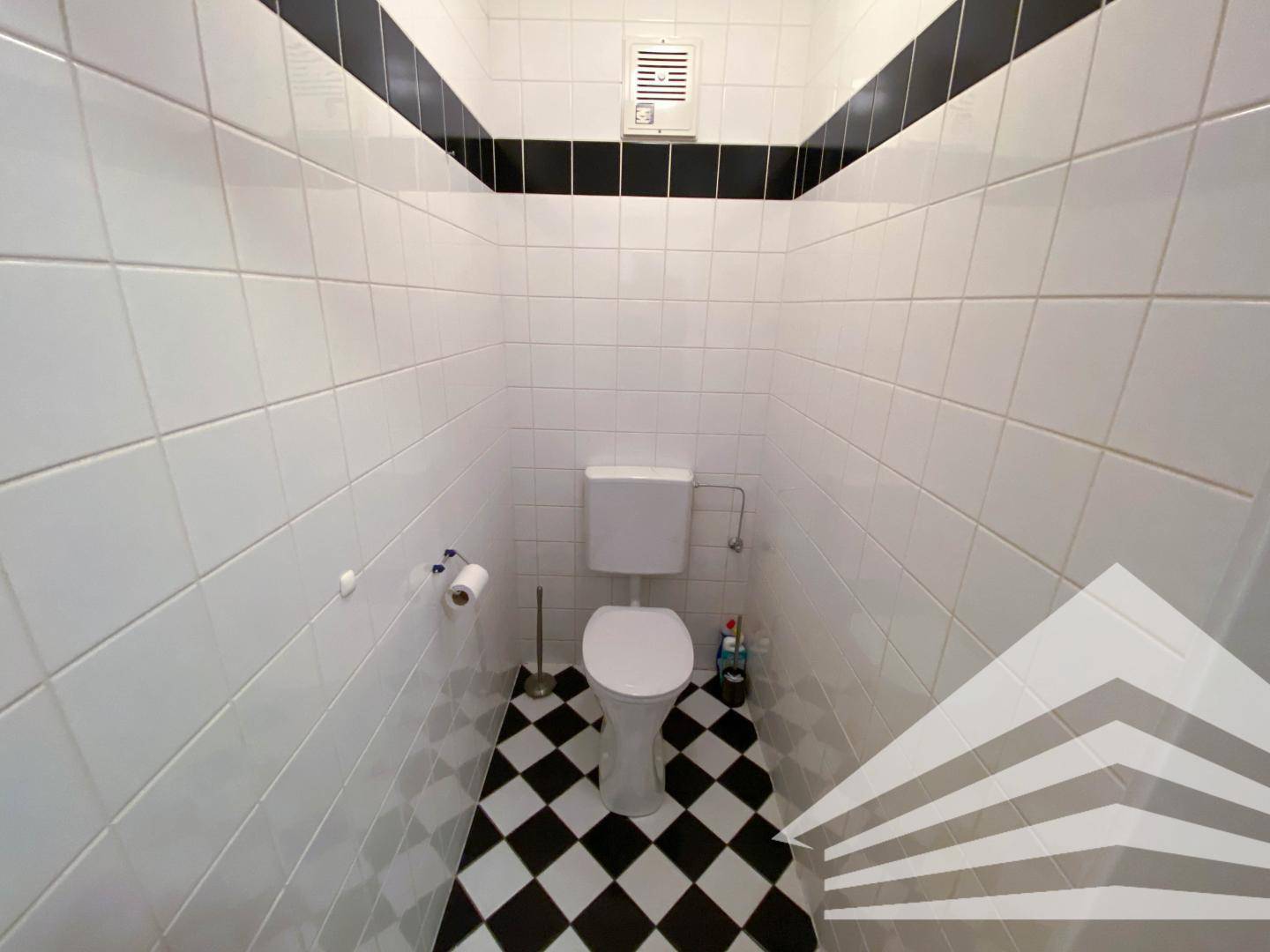Separates WC mit Toilette und auffälligen schwarz-weiß karierten Fliesen, sauber und funktional.
