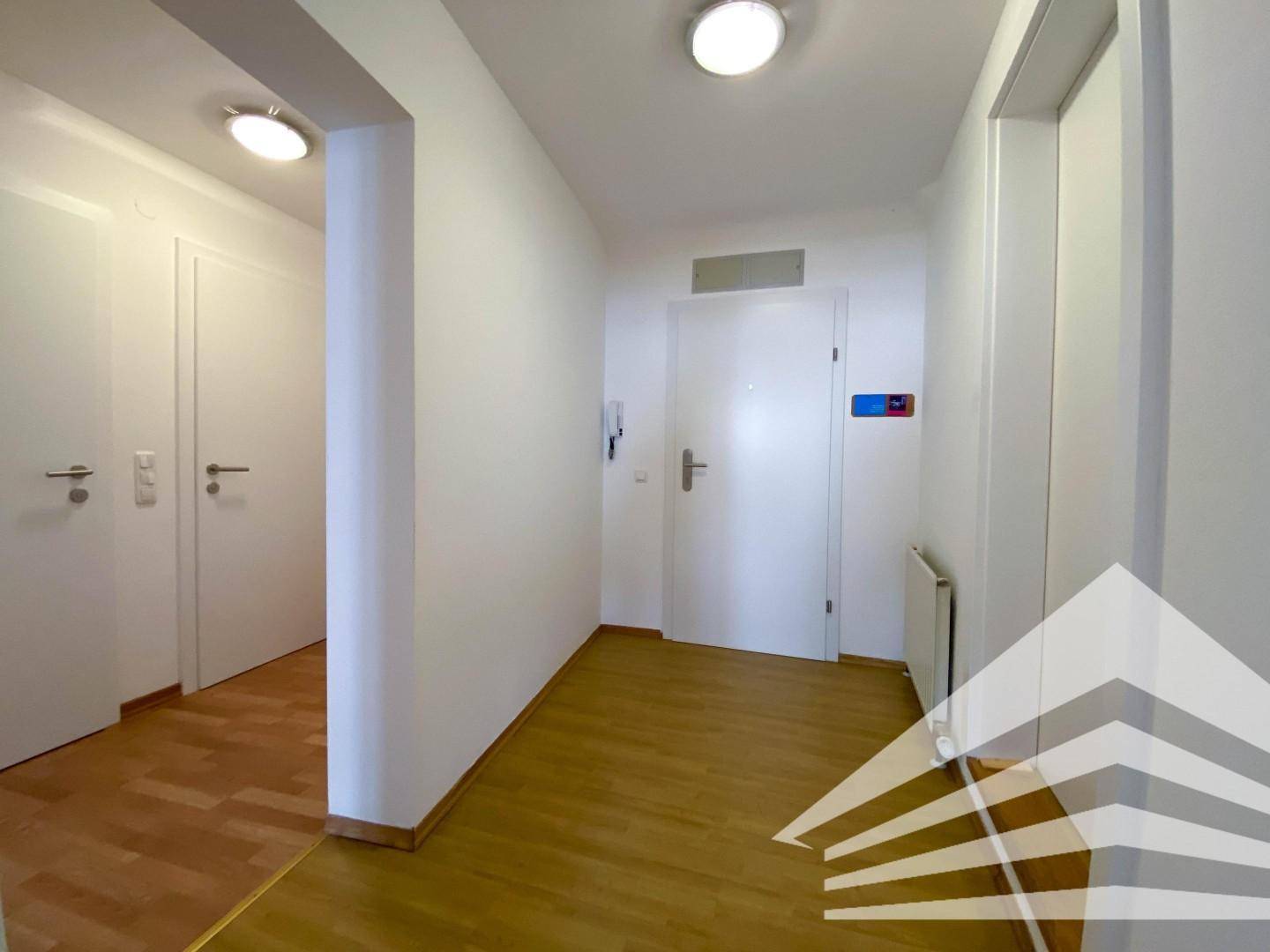 Heller Flur einer Wohnung mit Holzboden und weißen Türen, der zu weiteren Räumen führt.