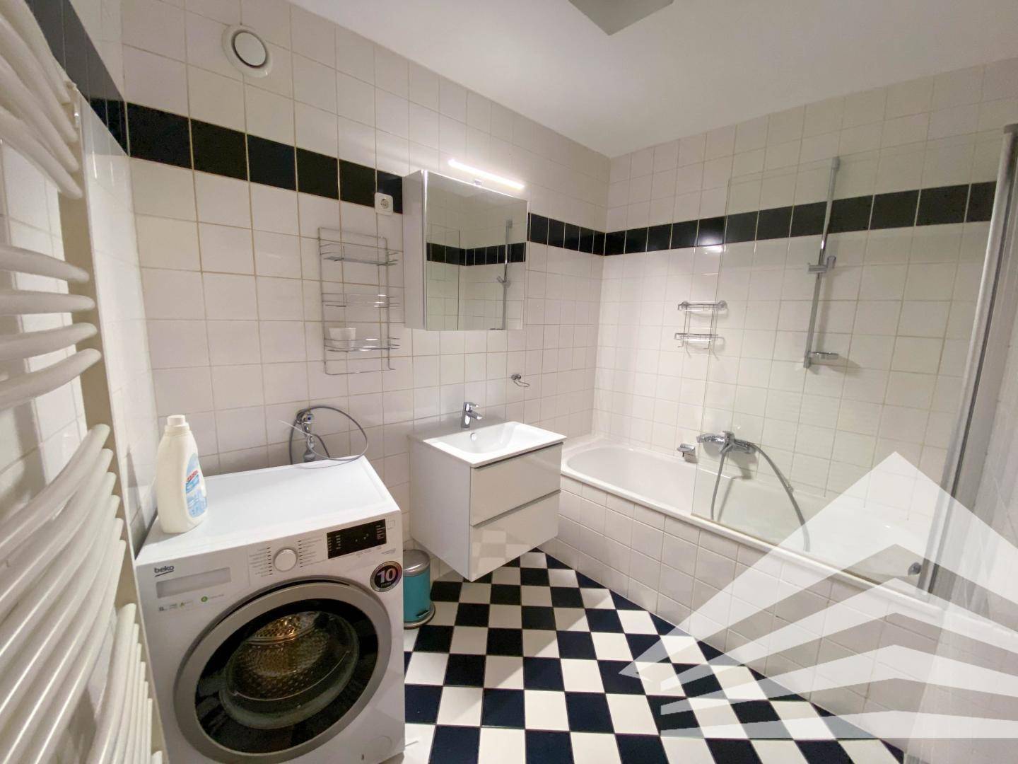 Badezimmer mit Badewanne, Waschbecken, Waschmaschine und markanten schwarz-weiß karierten Fliesen.