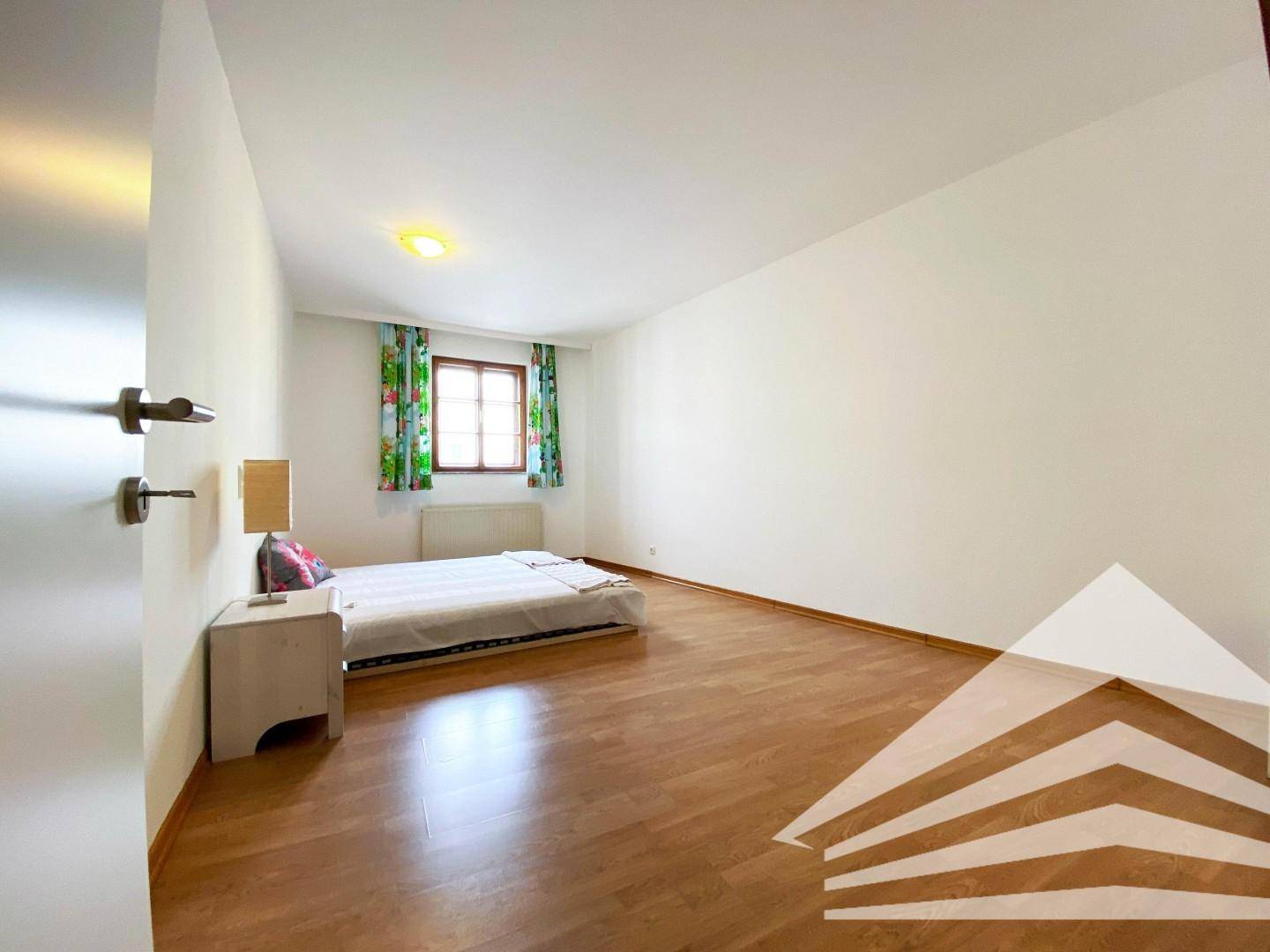 Helles Schlafzimmer mit Holzboden und einem Fenster, das eine angenehme Atmosphäre schafft.