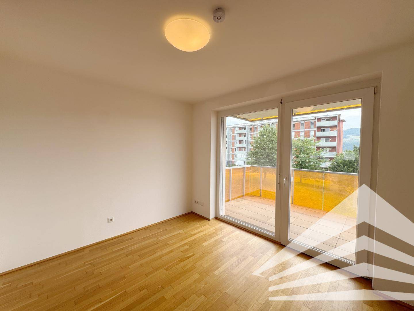 Geräumiger Raum mit Parkettboden und großem Balkonzugang, der viel Tageslicht hereinlässt.