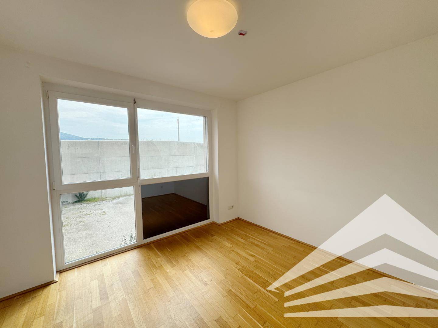 Helles Schlafzimmer mit Parkettboden und großem Fenster, das viel Tageslicht bietet.
