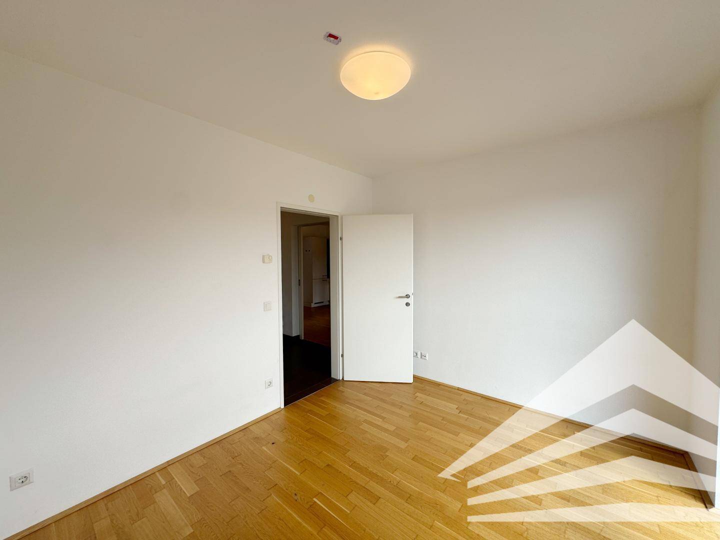 Leeres Schlafzimmer mit Parkettboden und weiß gestrichenen Wänden, bereit zur individuellen Gestaltung.