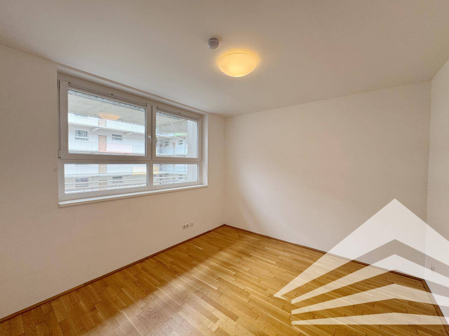 Schlafzimmer mit Parkettboden und Fenster, das einen Blick auf die umliegenden Gebäude ermöglicht.