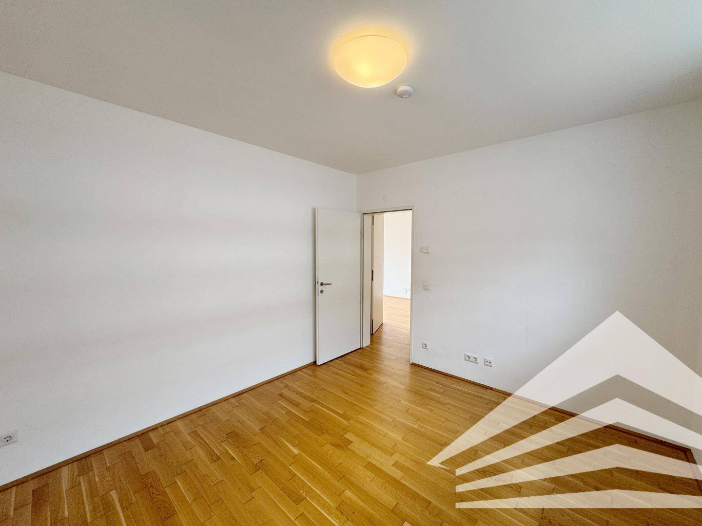 Leeres Schlafzimmer mit Parkettboden und weiß gestrichenen Wänden, ideal für persönliche Einrichtung.