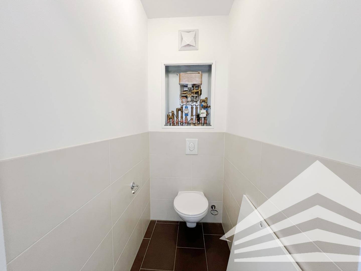 Separates WC mit wandhängender Toilette und sichtbaren Installationen in einer Nische.