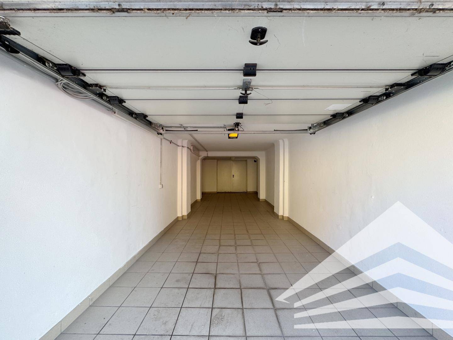 Langer Garagenstellplatz mit hellen Fliesen und weiß gestrichenen Wänden, bereit zur Nutzung.