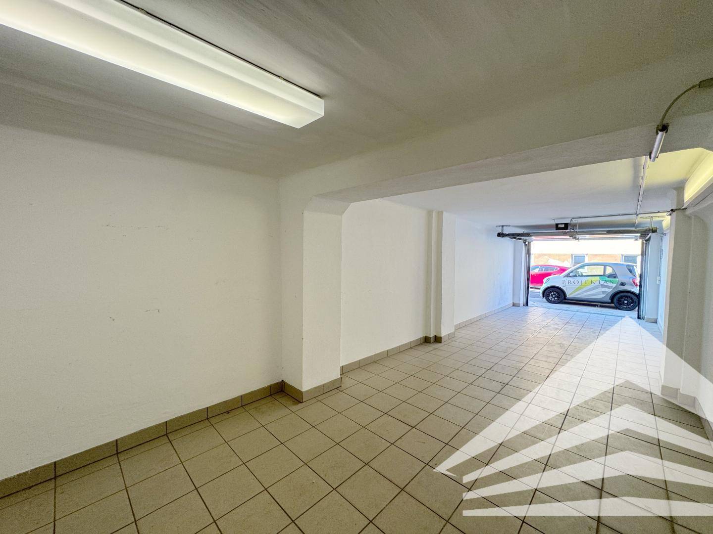 Heller Garagenraum mit Fliesenboden und Blick auf die Einfahrt, geeignet für ein Auto.