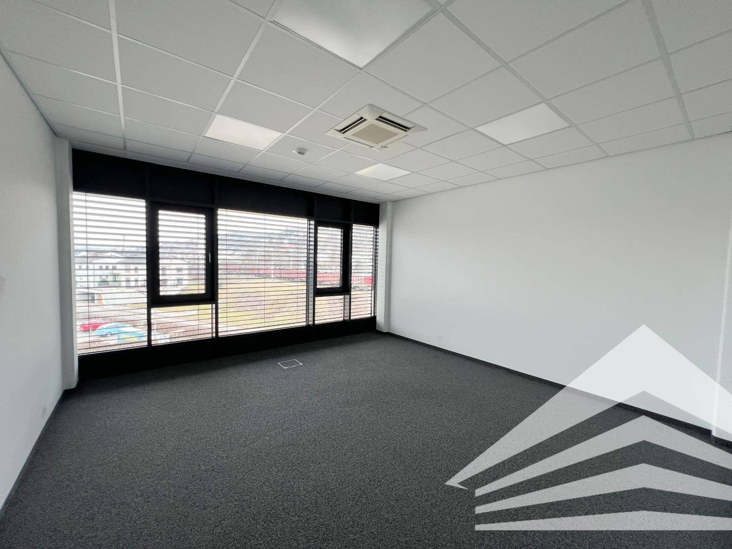 Geräumiges, leeres Büro mit Teppichboden und breiter Fensterfront für viel Tageslicht.