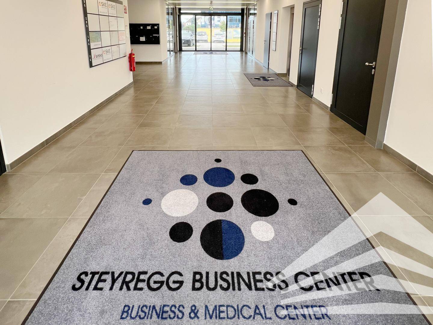 Heller Eingangsbereich eines Business Centers mit Fliesenboden und Firmenlogo auf dem Teppich.