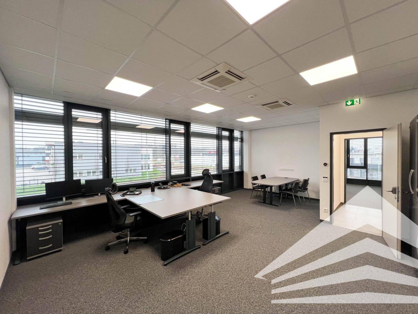 Geräumiges Büro mit Teppichboden, mehreren Arbeitsplätzen und einem kleinen Besprechungsbereich.