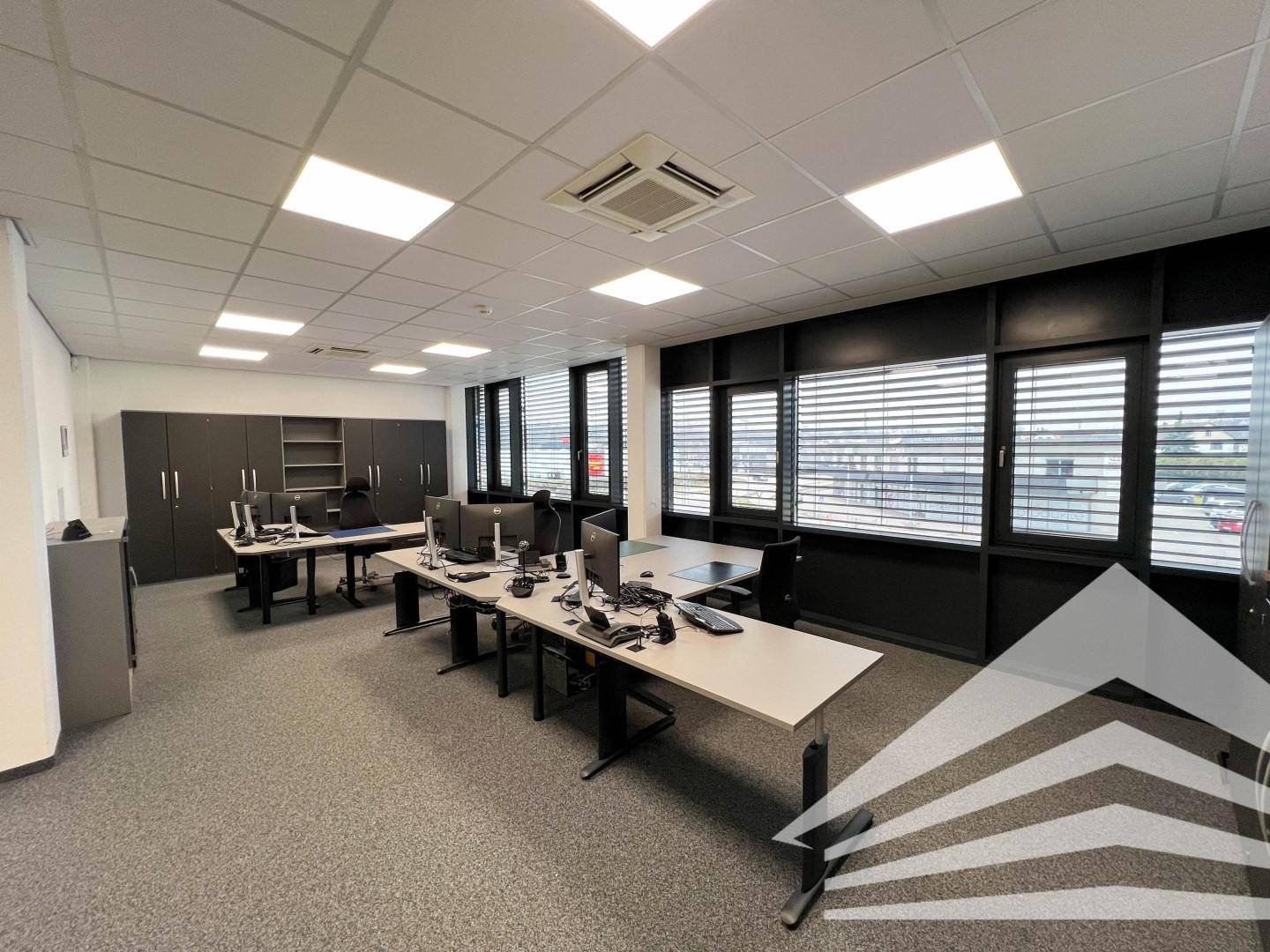 Geräumiges Büro mit Teppichboden, dunklen Schränken und mehreren Arbeitsplätzen, gut beleuchtet.