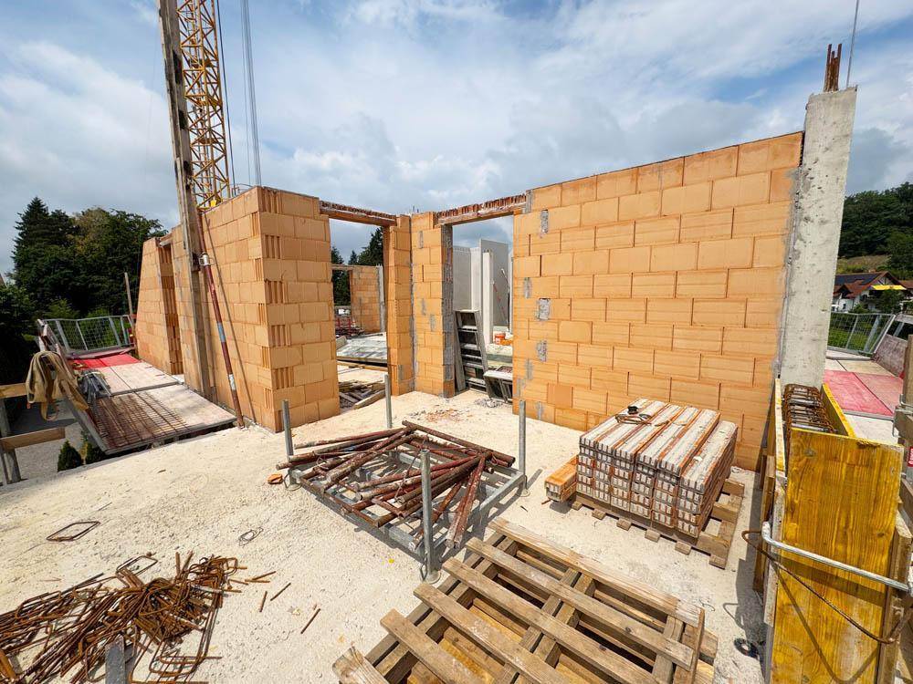 Innenansicht eines Rohbaus mit Ziegelwänden und Baumaterialien auf dem Betonboden.