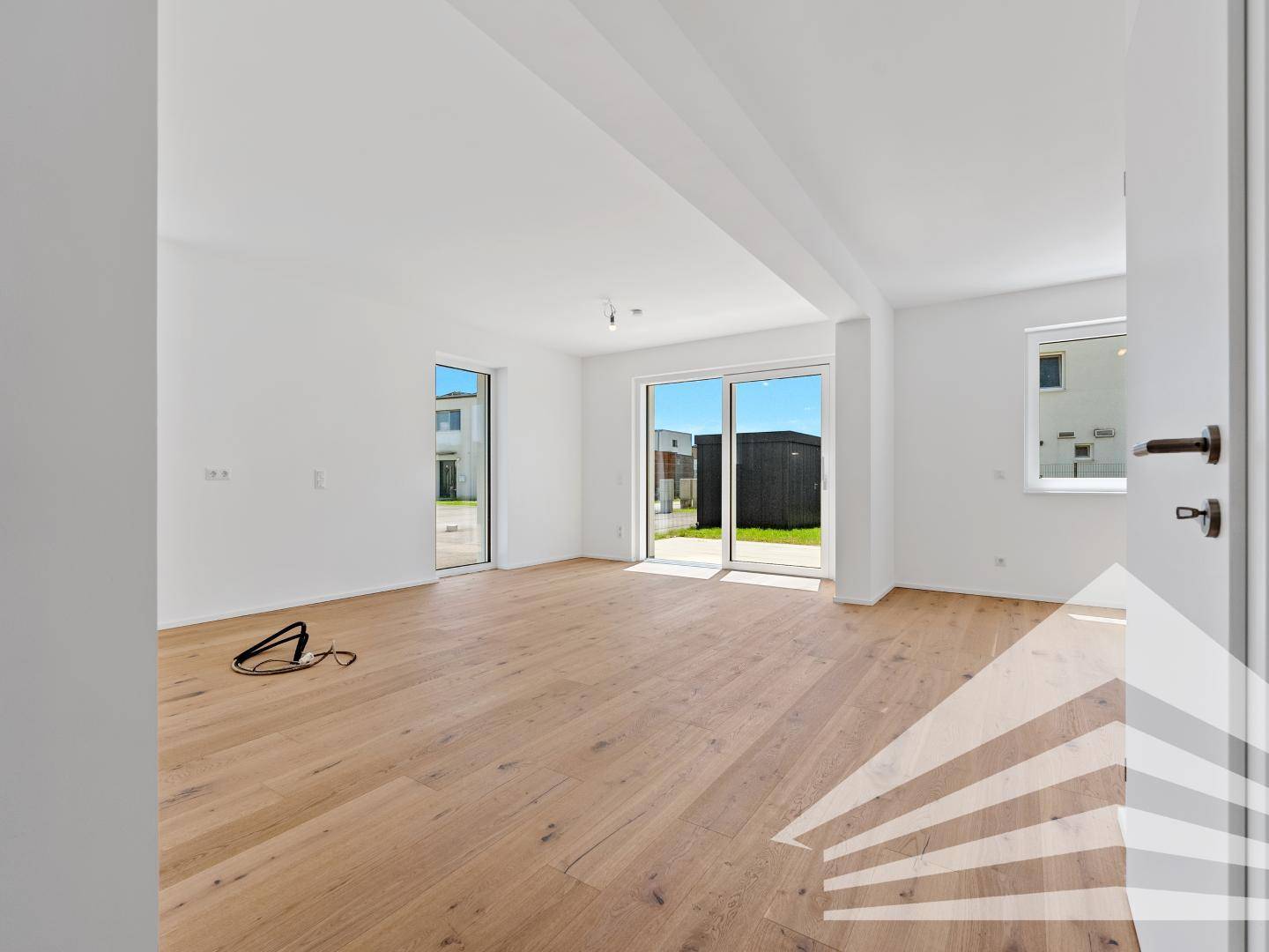 Geräumiges, leeres Wohnzimmer mit Holzboden und großen Schiebetüren zum Gartenbereich.
