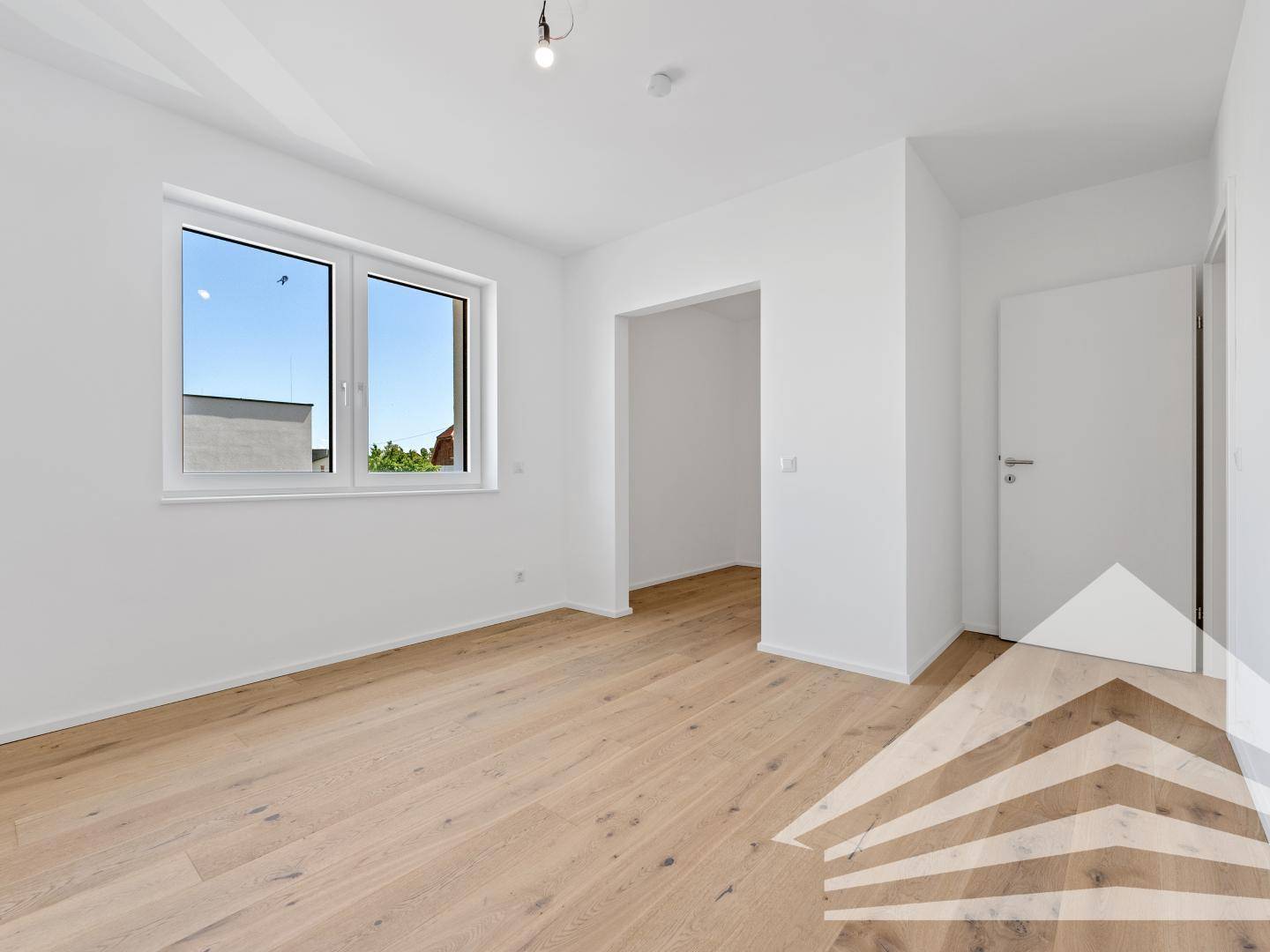 Helles, leeres Schlafzimmer mit Holzboden und Zugang zu einem weiteren Raum.