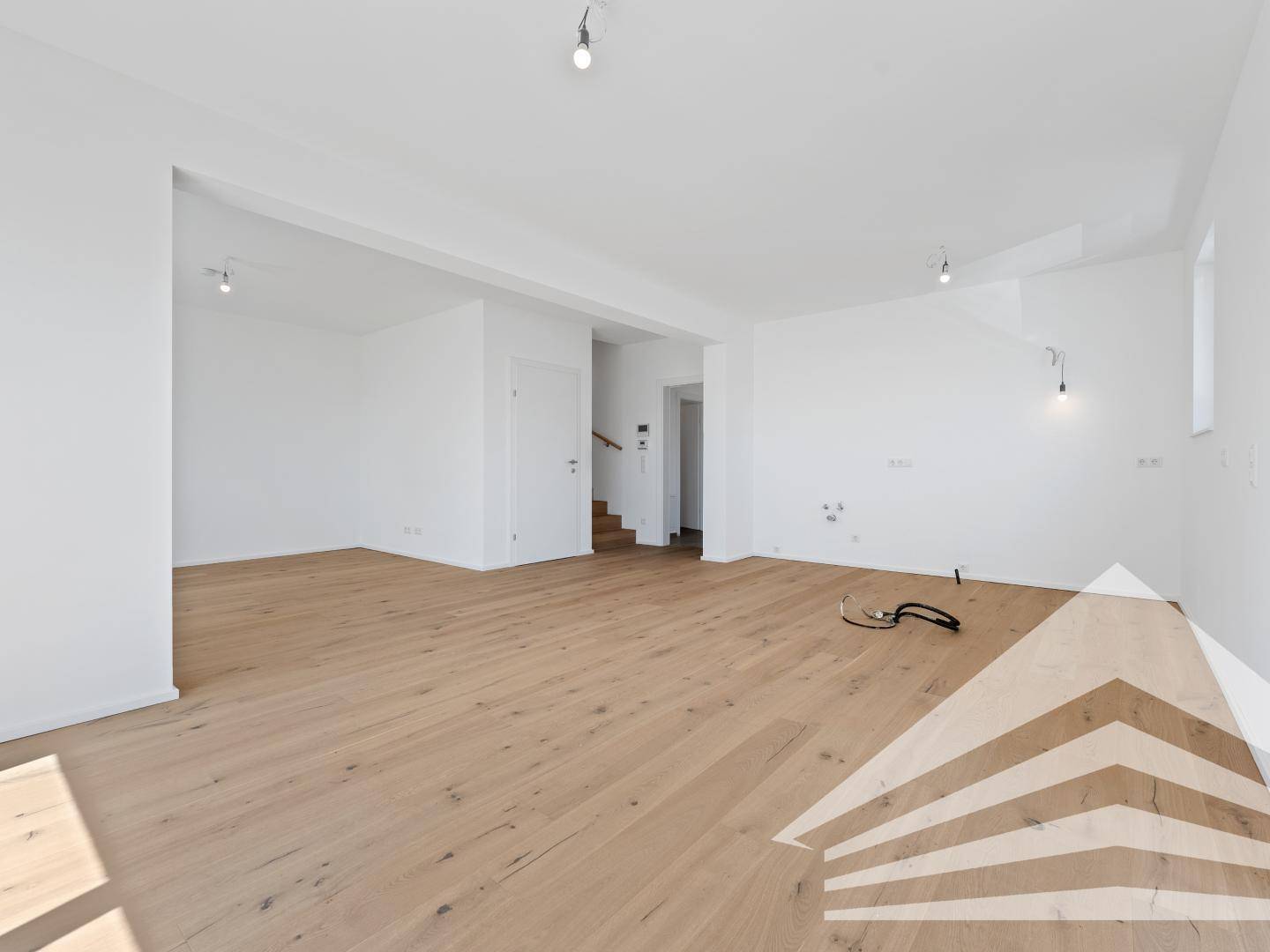Geräumiger, leerer Wohnbereich mit Holzboden und offener Treppe zum Obergeschoss.