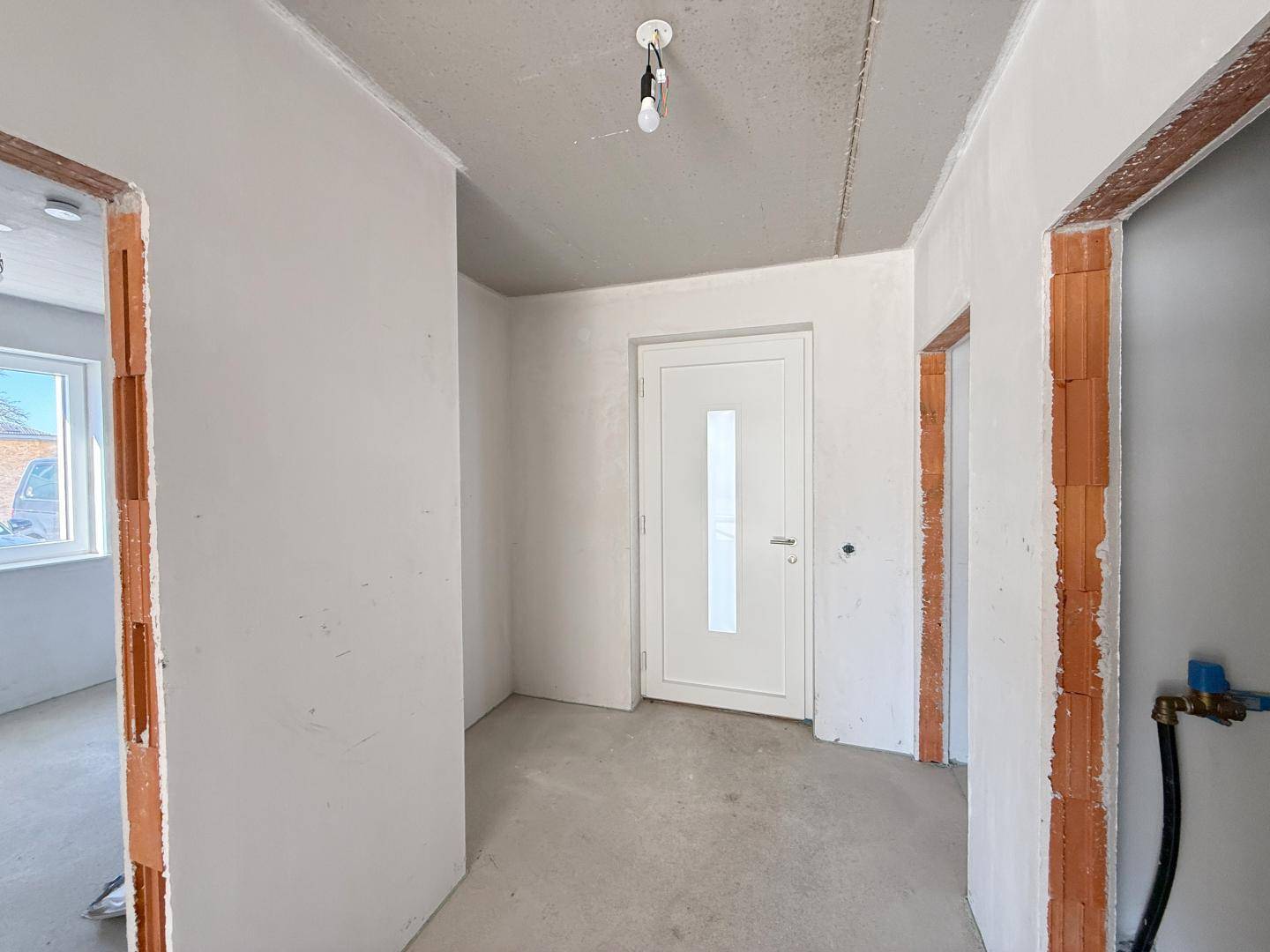 Eingangsbereich im Rohbau mit einer modernen weißen Tür und Zugang zu weiteren Räumen.