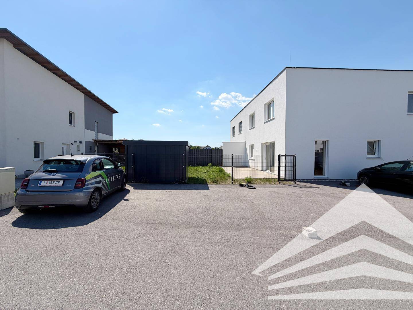 Außenbereich mit Parkplätzen und einem kleinen Garten hinter dem Gebäude.