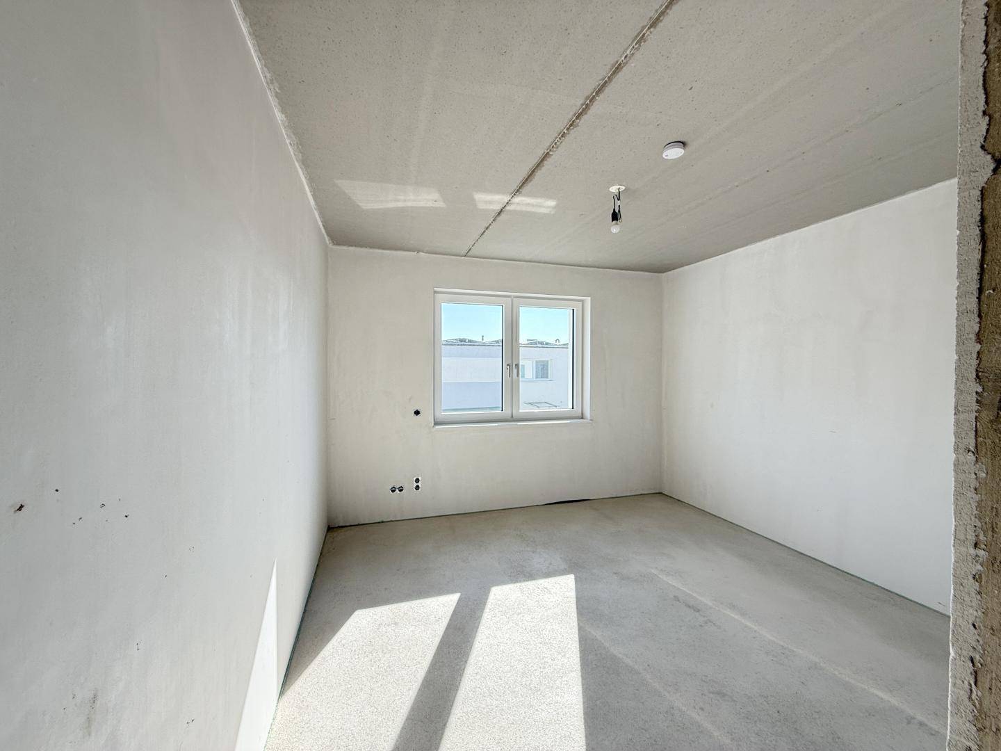 Unfertiger Raum mit Fenster und Betonboden, wartet auf den finalen Ausbau.