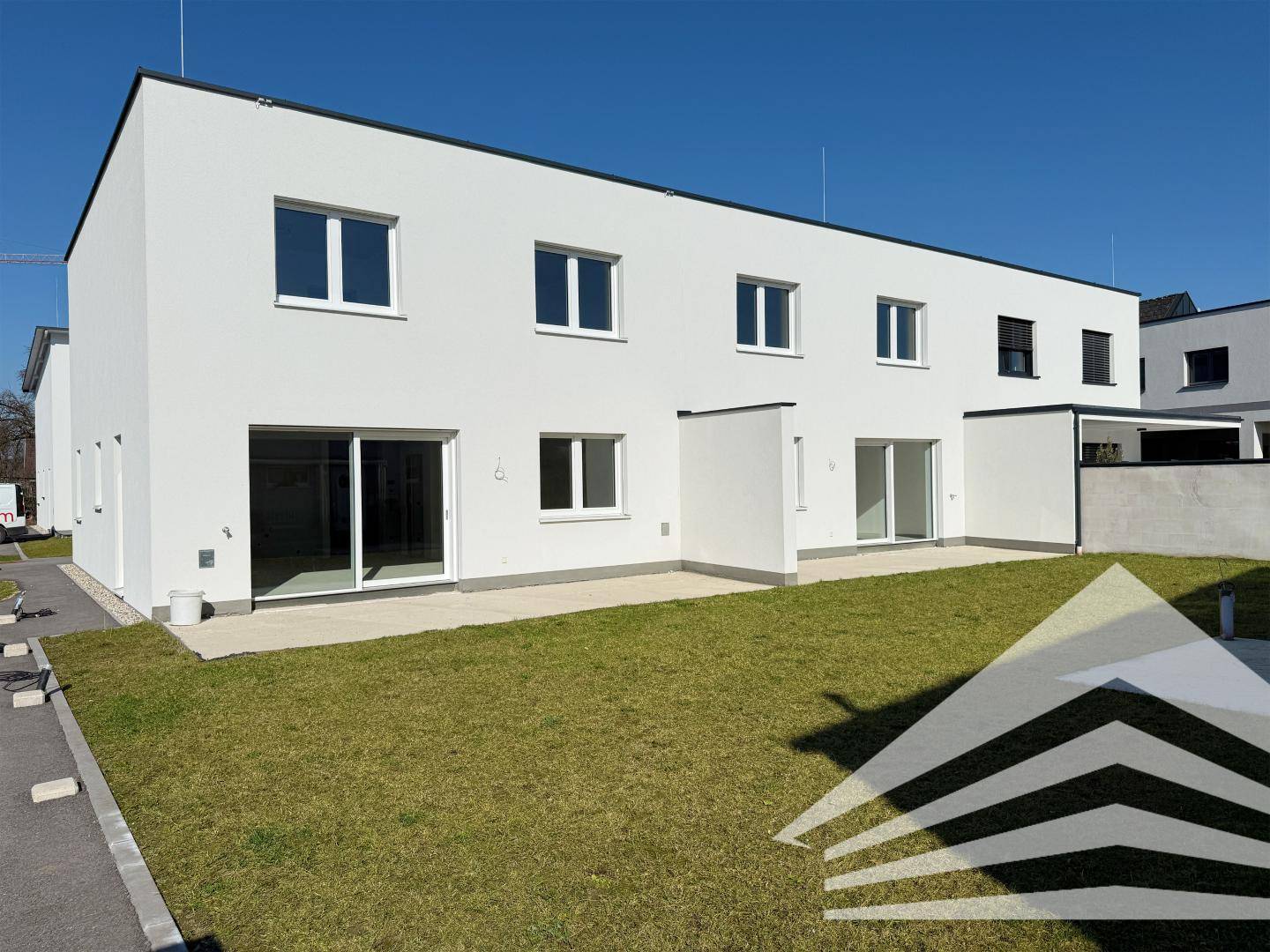 Moderne weiße Reihenhäuser mit grüner Rasenfläche und privater Terrasse.
