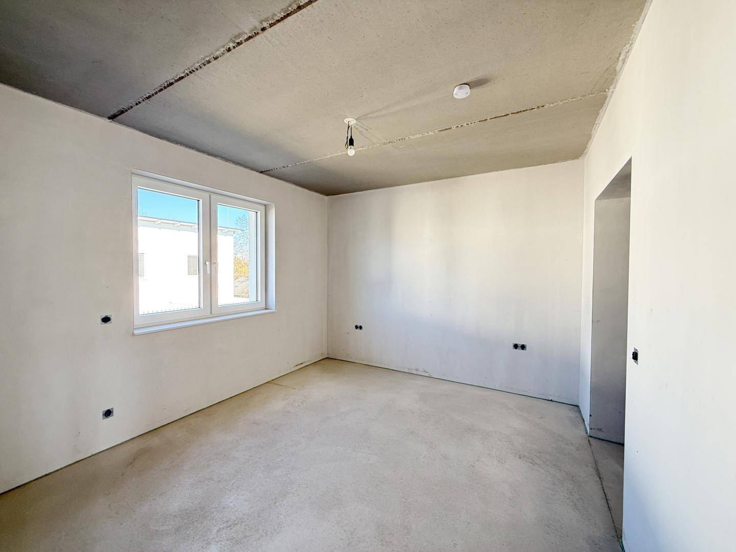 Heller, unfertiger Raum mit Fenster und Betonboden, ideal für individuelle Gestaltung.