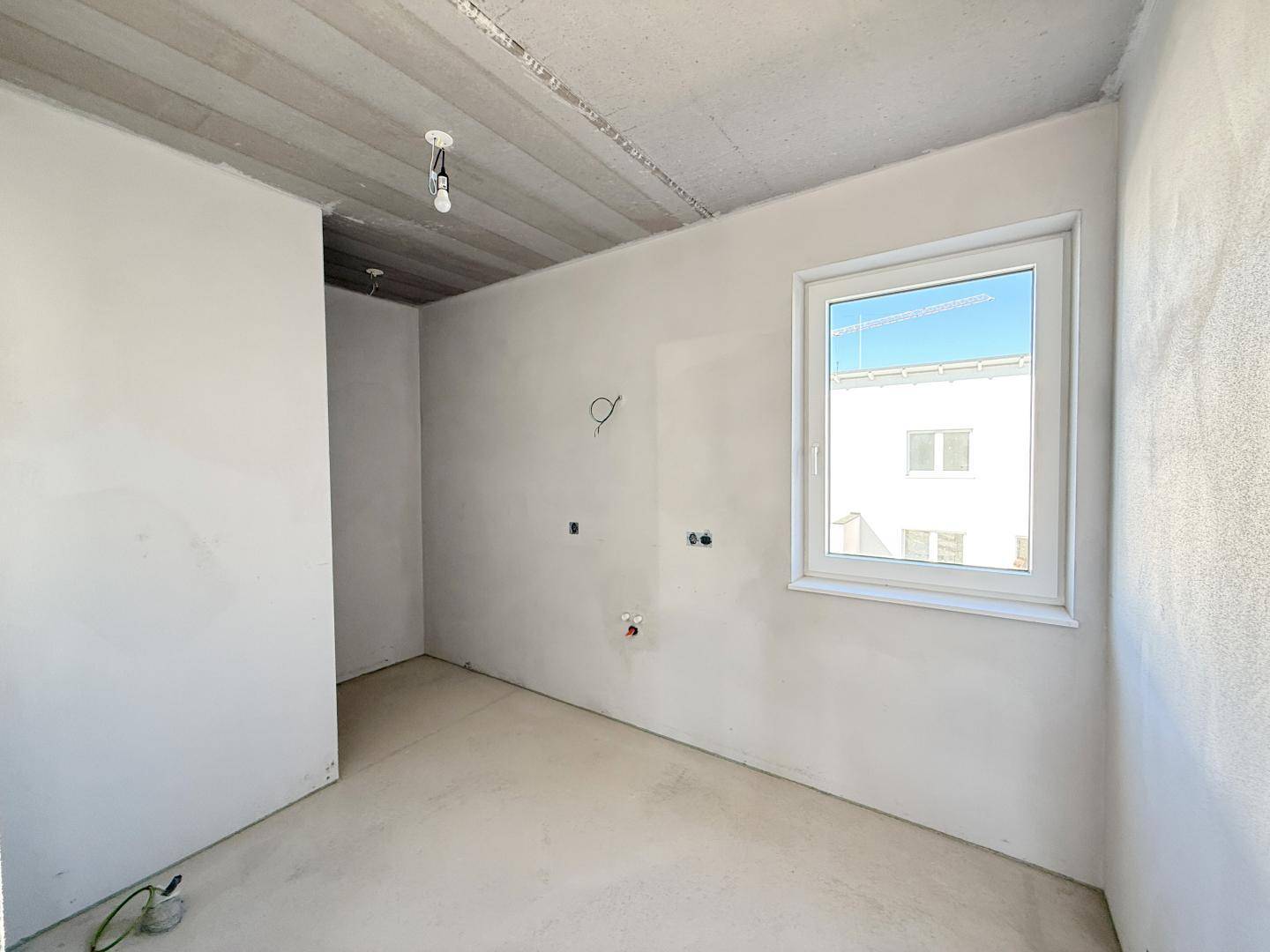Unfertiger Raum mit Fenster und sichtbaren Anschlüssen, bereit für Bad oder Küche.