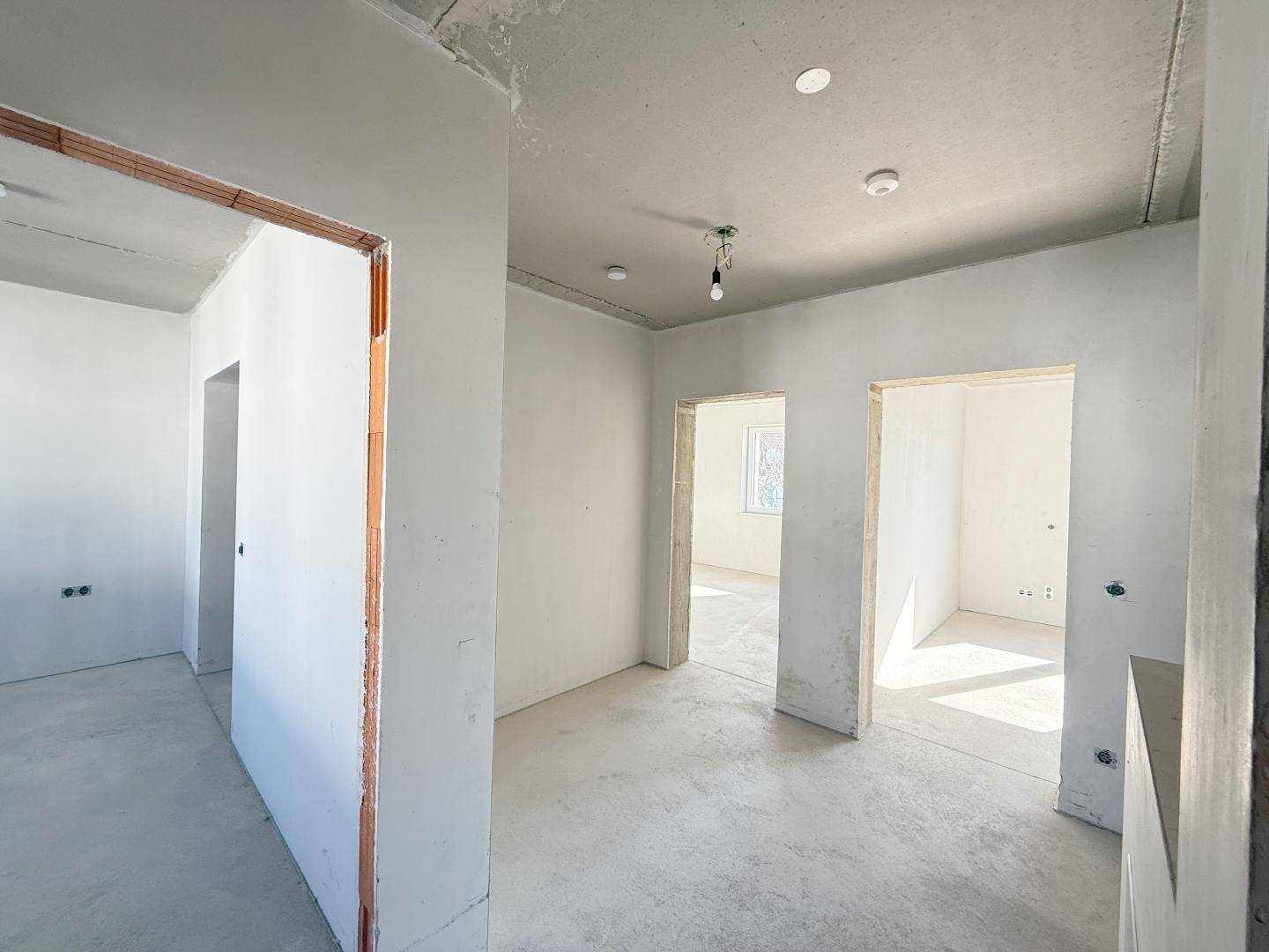 Unfertiger Flur mit mehreren Türöffnungen und Betonboden, bereit für den Innenausbau.