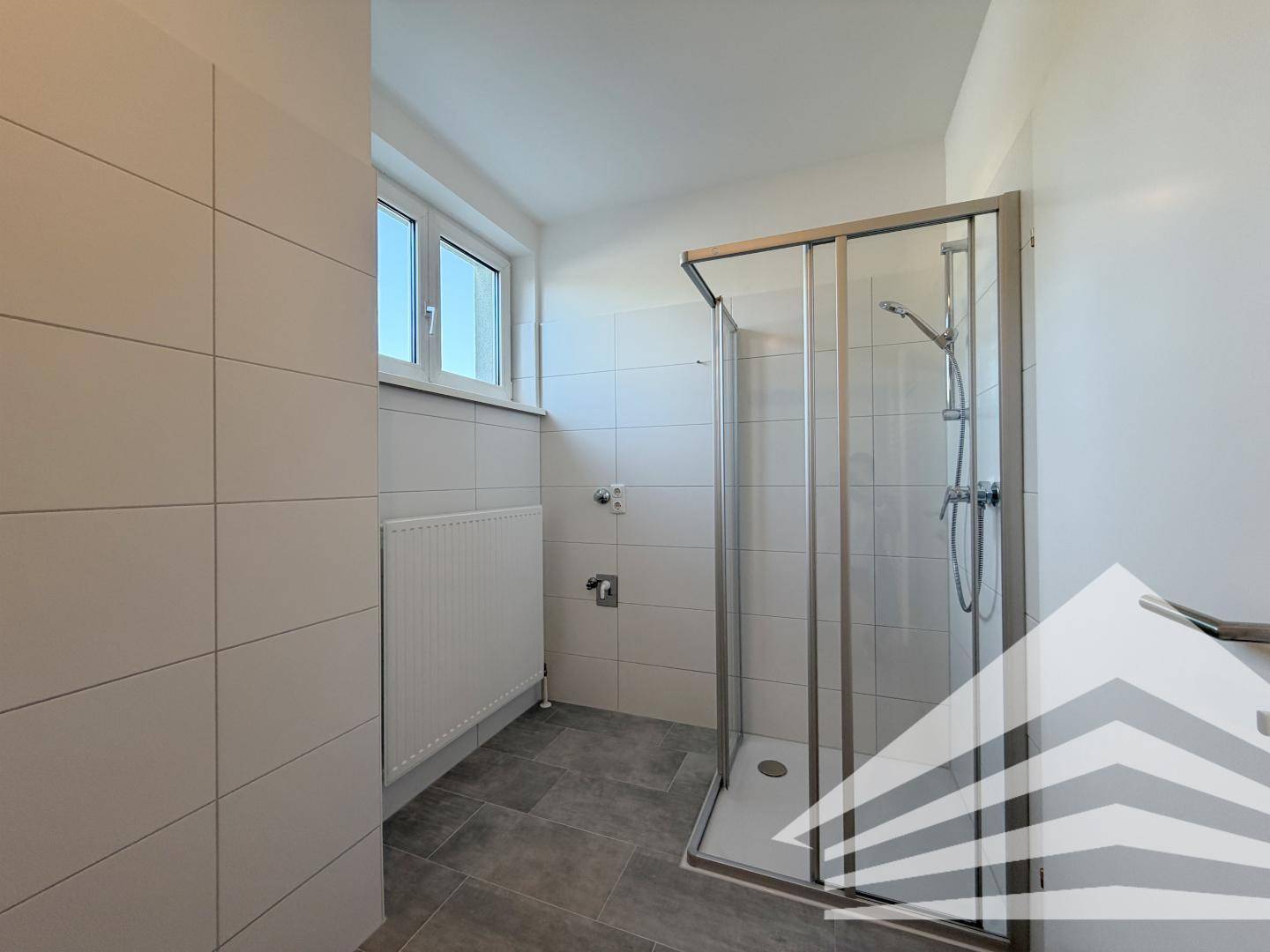Helles Badezimmer mit Dusche, Fenster und weißen Fliesen.