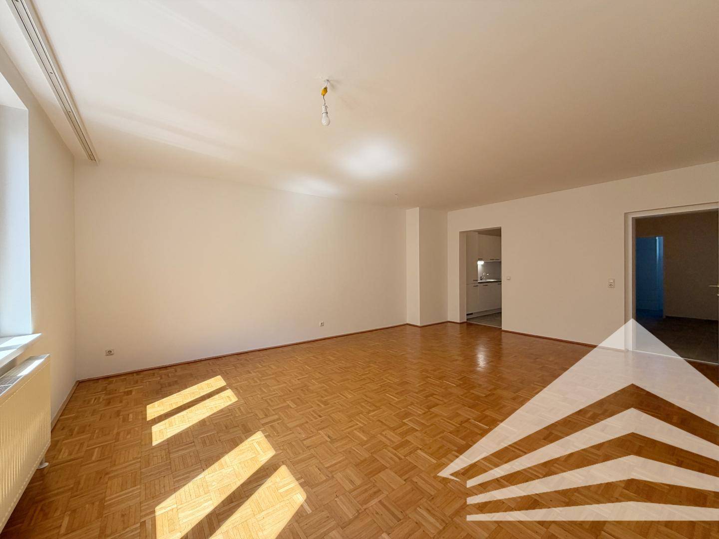 Helles Wohnzimmer mit Parkettboden und Zugang zu weiteren Räumen.