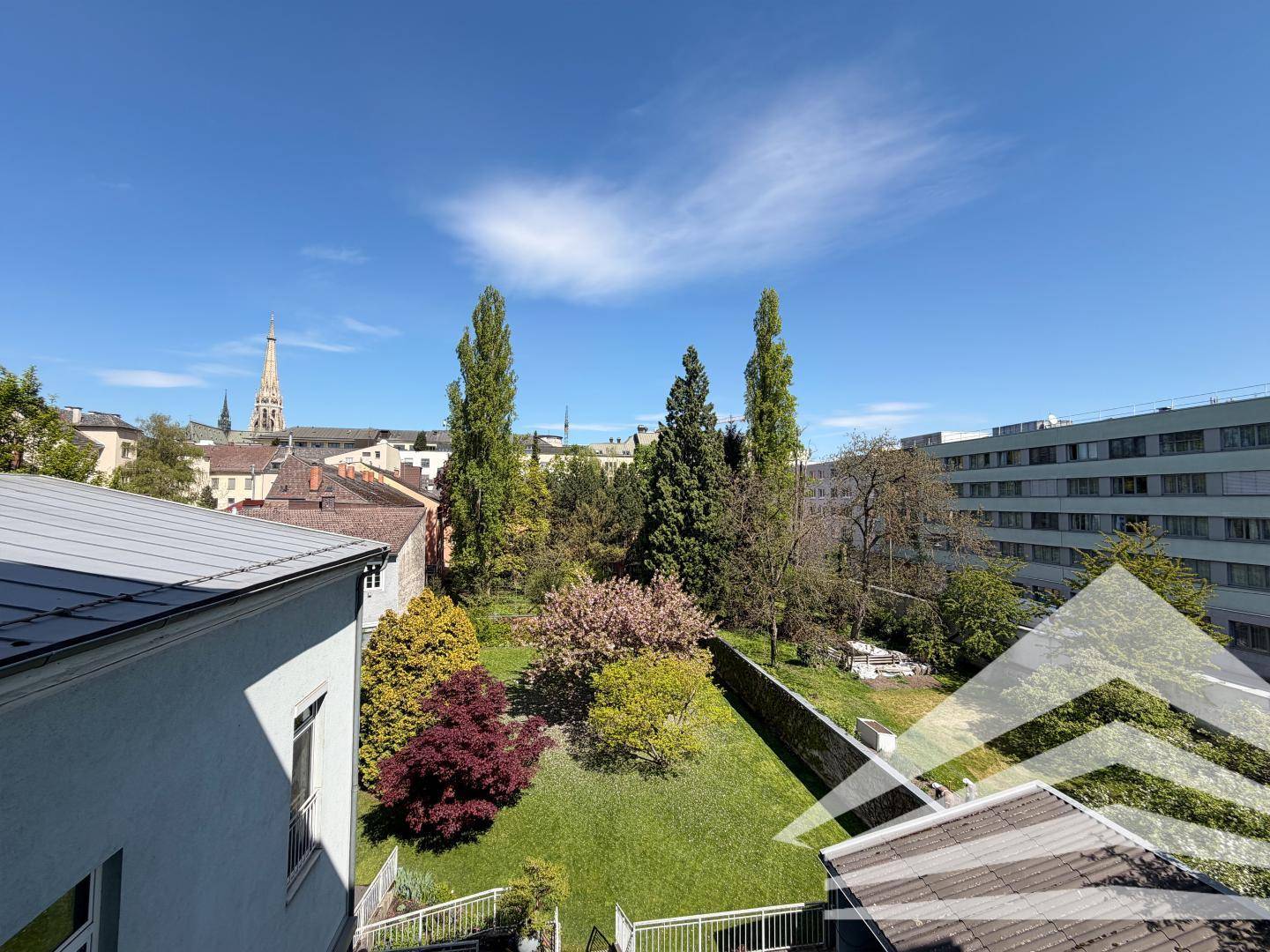 Weitläufiger Blick über einen grünen Garten und die Dächer der Stadt.