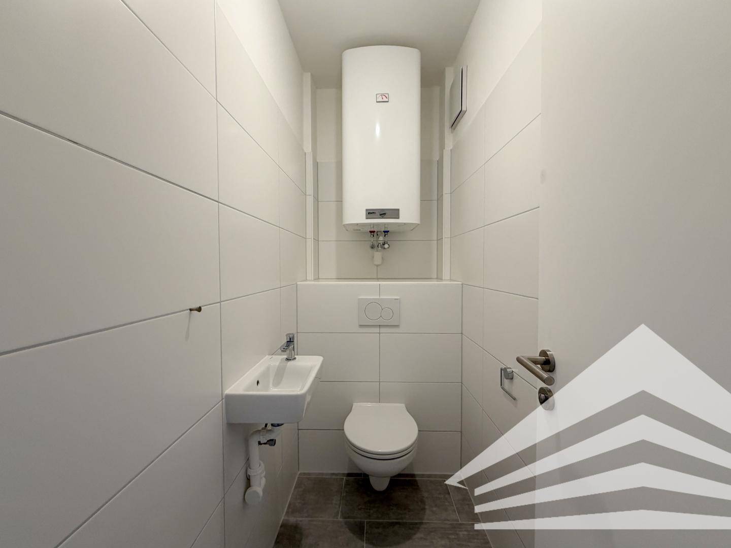 Separates WC mit wandhängender Toilette, kleinem Waschbecken und Boiler.
