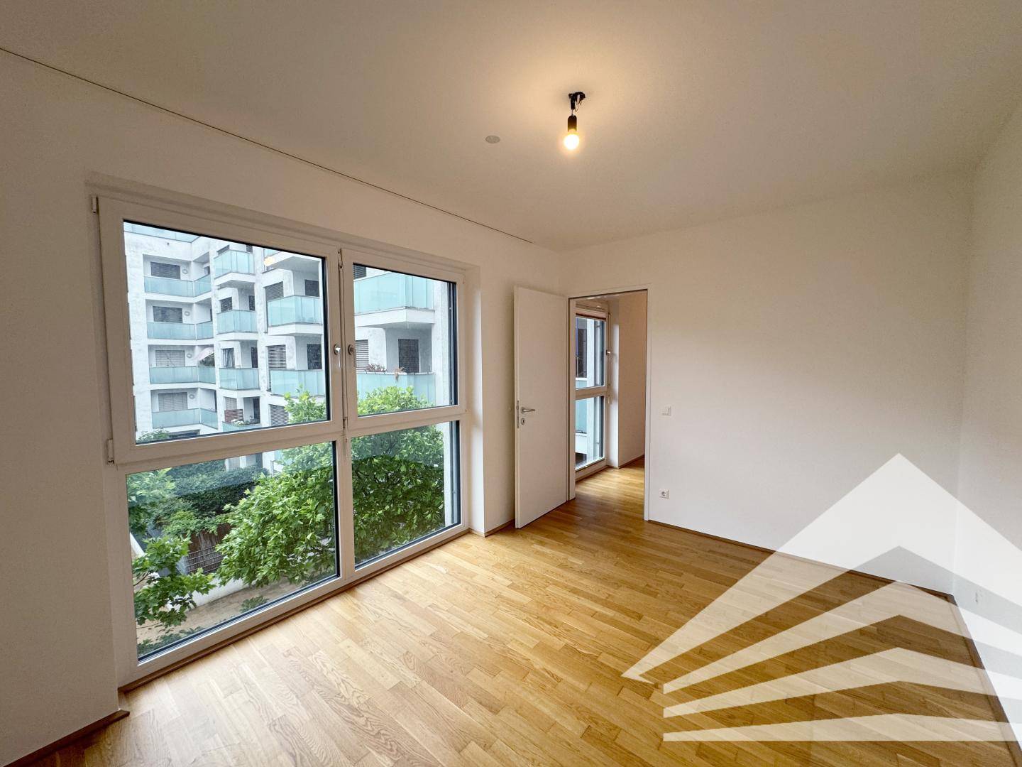 Helles Zimmer mit Parkettboden und großen Fenstern, die einen grünen Ausblick bieten.
