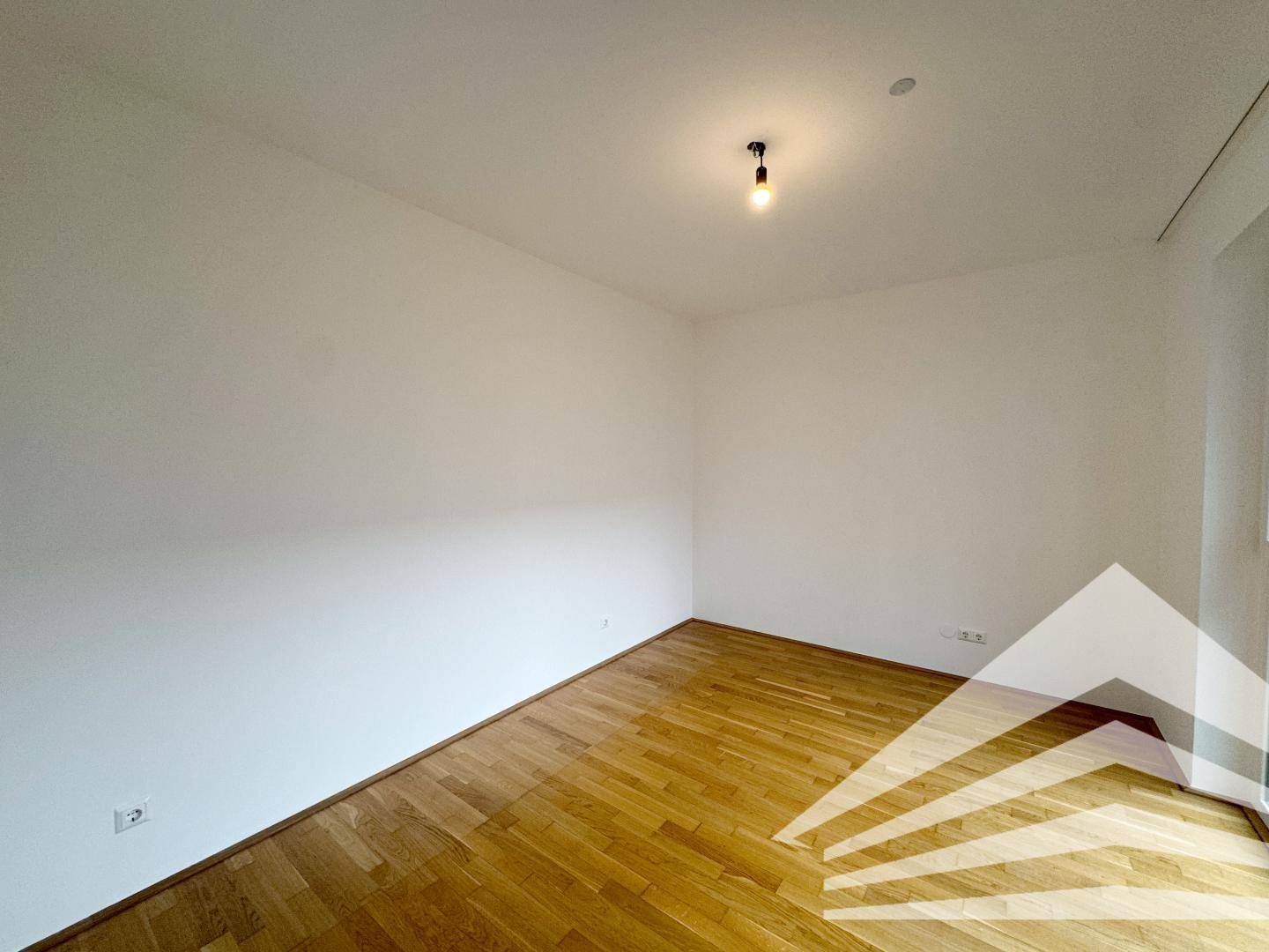 Schlichtes Zimmer mit Parkettboden und weißen Wänden, bereit zur individuellen Gestaltung.