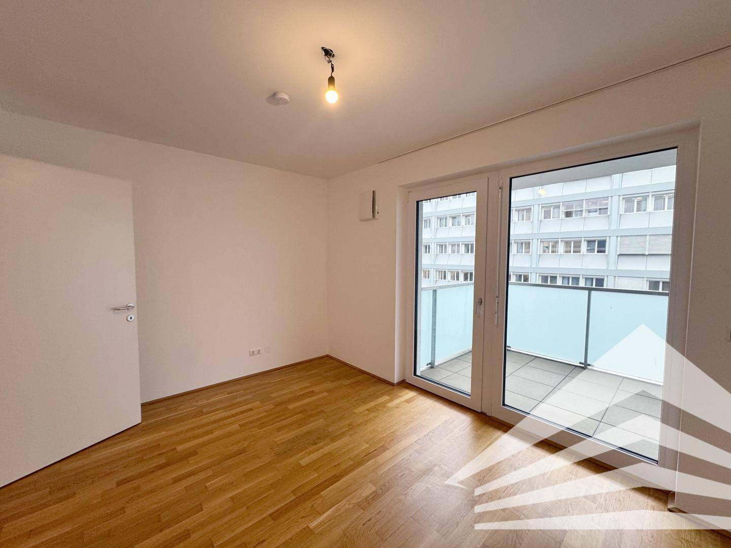 Helles Zimmer mit Parkettboden und großem Balkonzugang, ideal als Schlafzimmer.