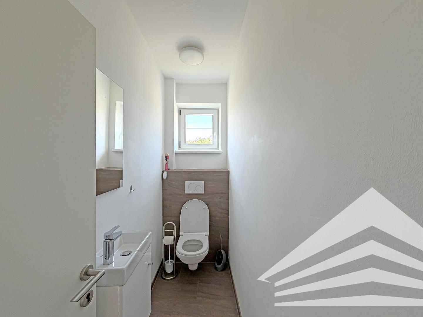 Modernes Gäste-WC mit wandhängendem WC, kleinem Waschbecken und einem Fenster für Tageslicht.