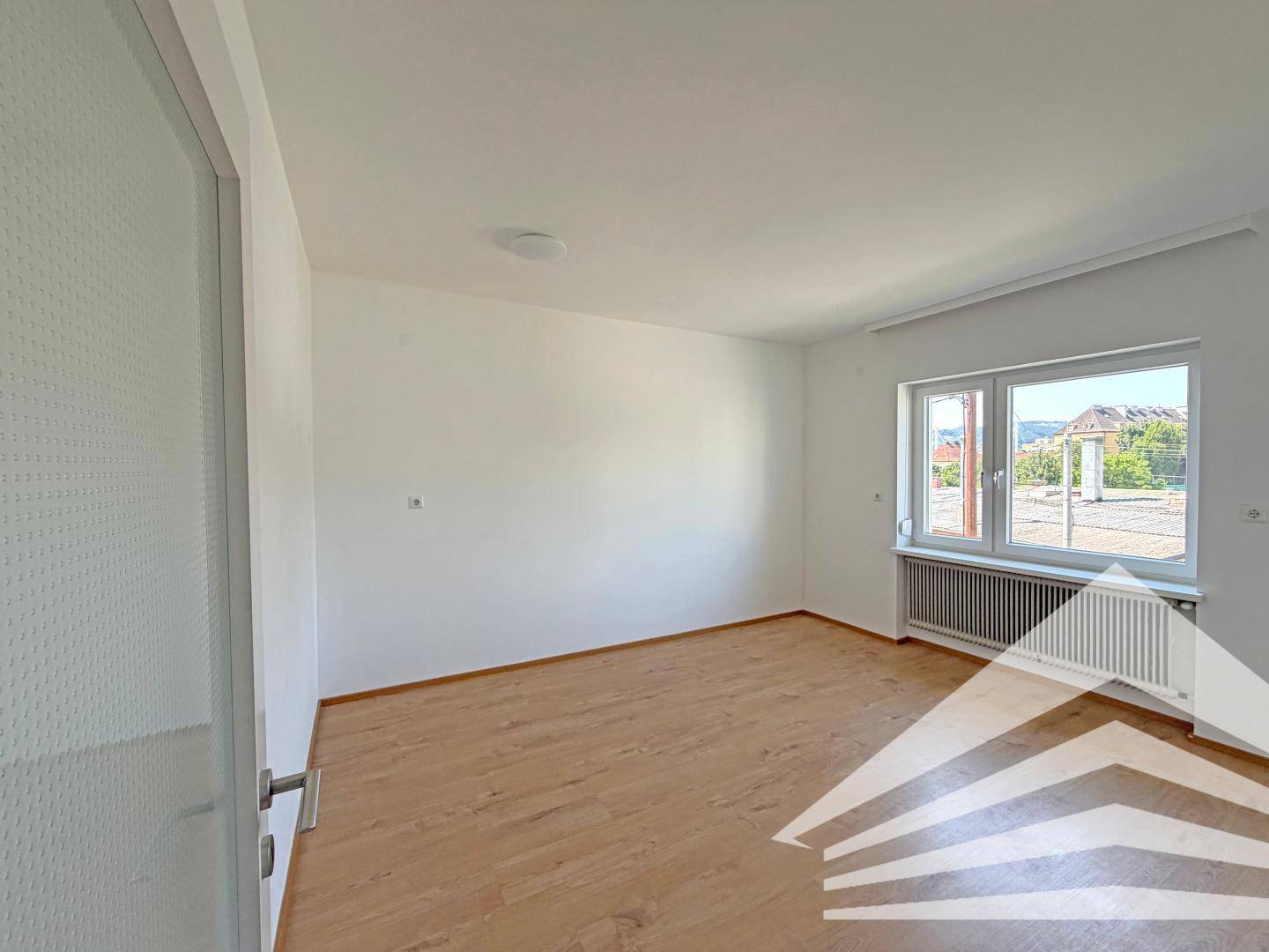 Geräumiges, helles Schlafzimmer mit Laminatboden und einem Fenster, das viel Tageslicht hereinlässt.