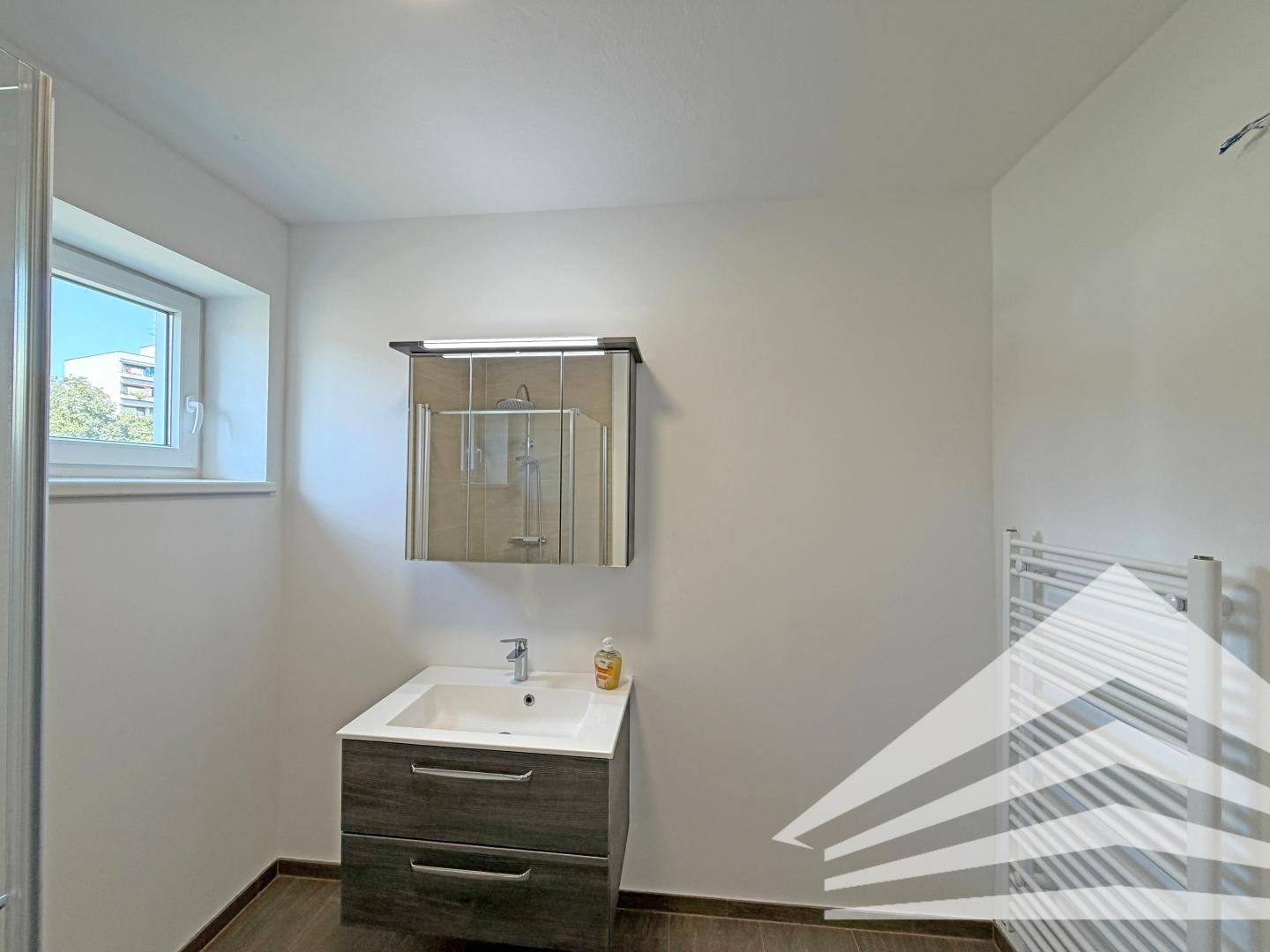 Modernes Badezimmer mit Waschtisch, Spiegelschrank und beheiztem Handtuchhalter neben der Dusche.