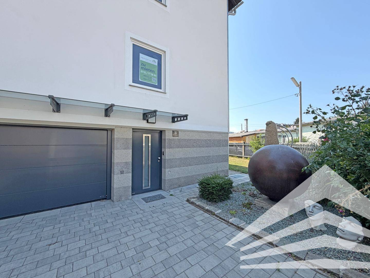 Moderner Hauseingang mit Vordach und integrierter Garage, umgeben von gepflastertem Bereich.