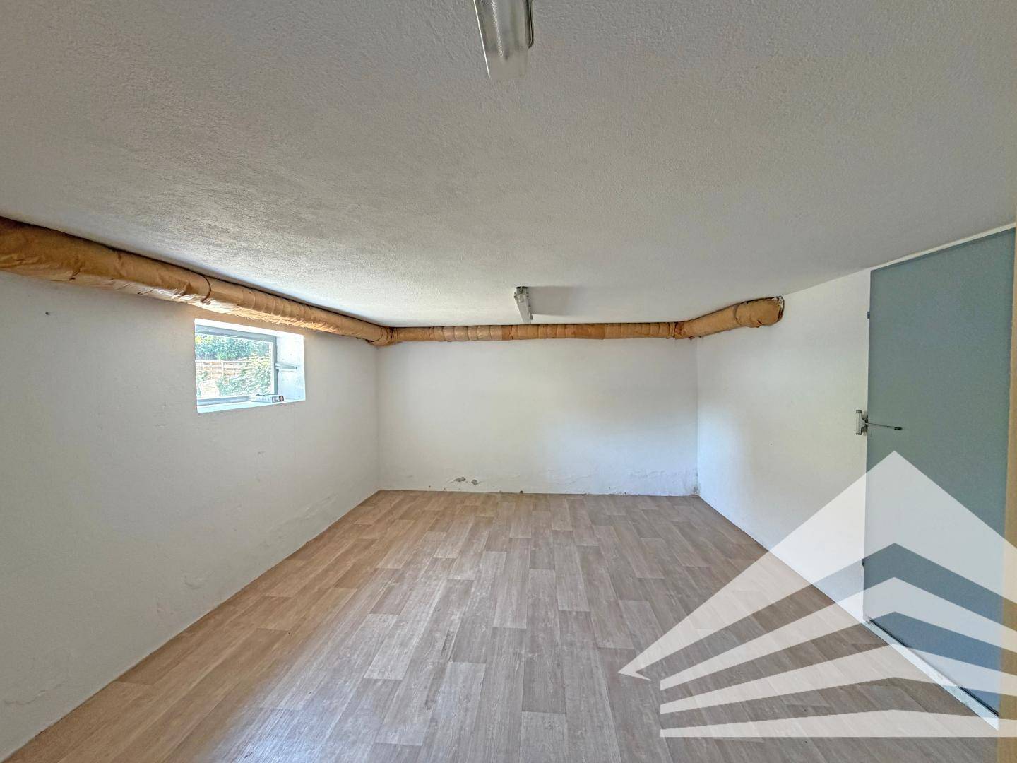Leerer Raum mit Laminatboden, weißen Wänden und einem kleinen Fenster, ideal als Abstell- oder Hobbyraum.